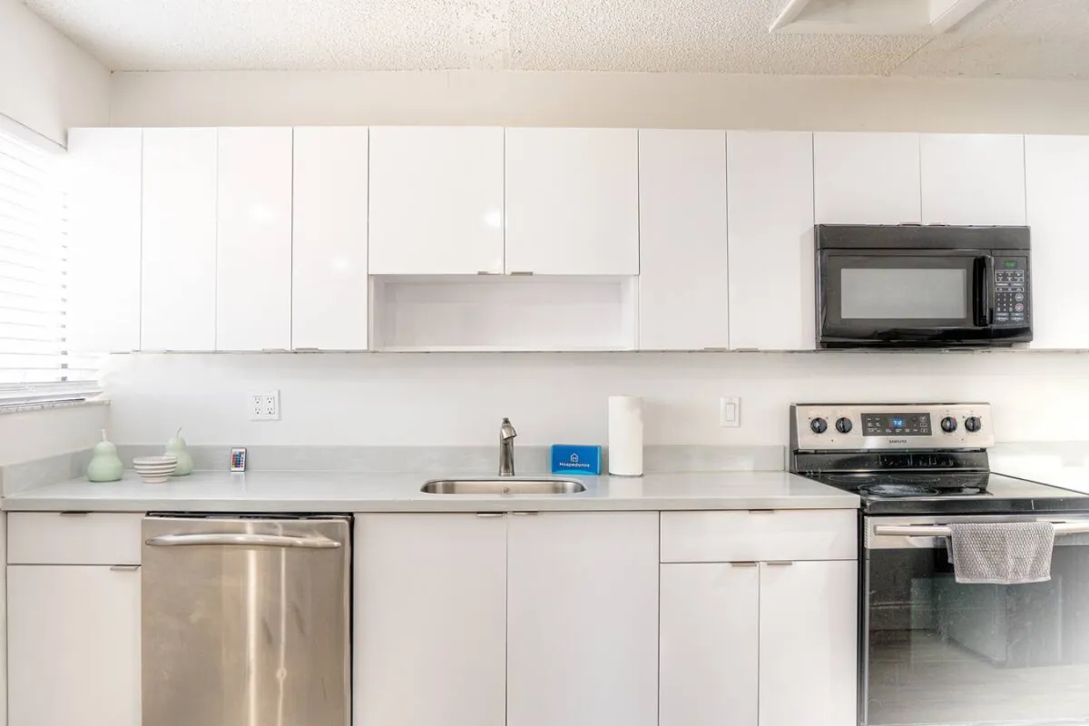 A contemporary kitchen scene highlighting stainless steel appliances, white cabinetry, and a welcoming countertop. The space is styled for both cooking and gathering, with subtle cues of social interaction and meal preparation.