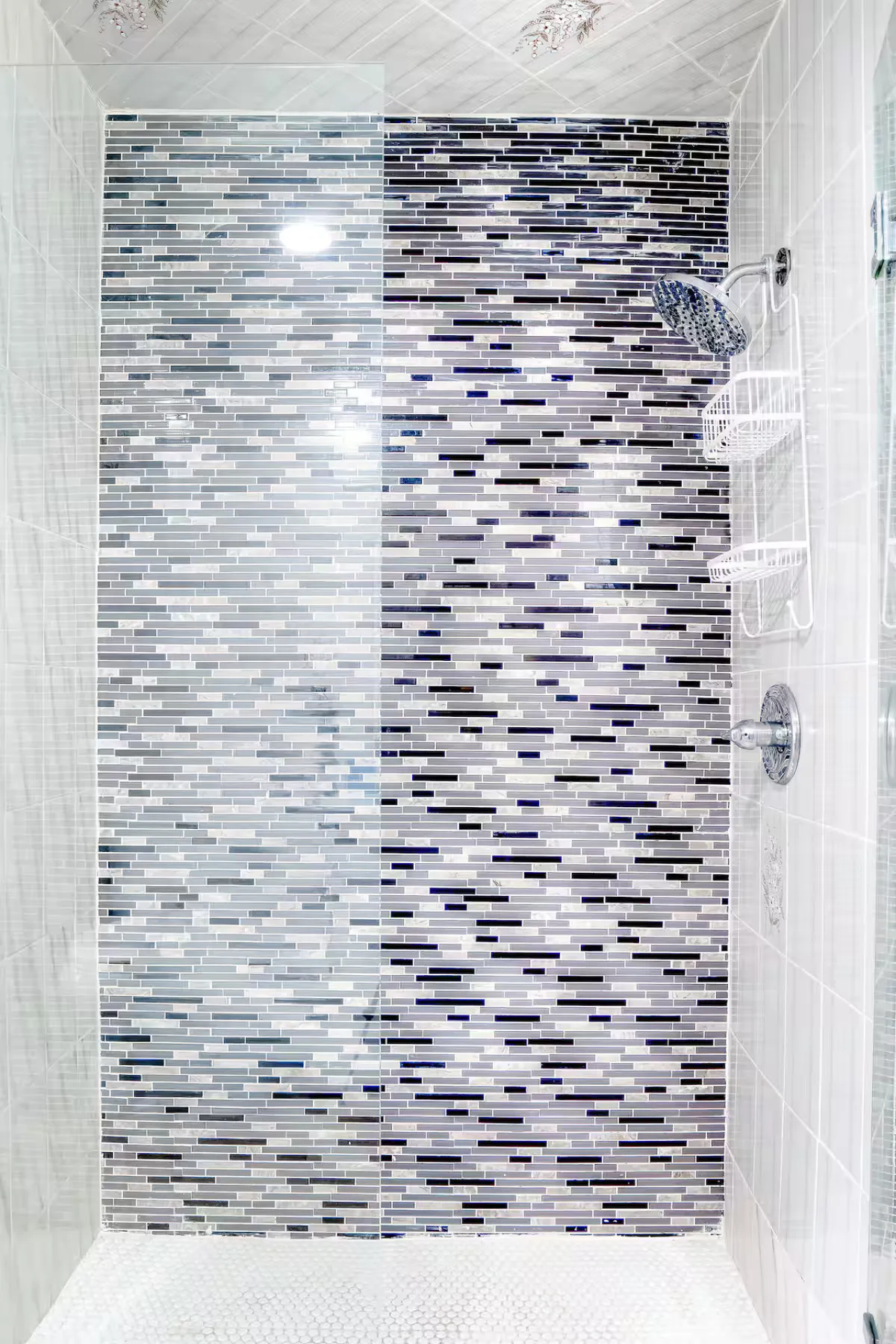 This image showcases a modern walk-in shower with a striking mosaic tile wall, a glass shower partition, and sleek chrome fixtures. The clean lines and contemporary design evoke a spa-like atmosphere, aligning perfectly with the description of a spa-inspired bathroom.